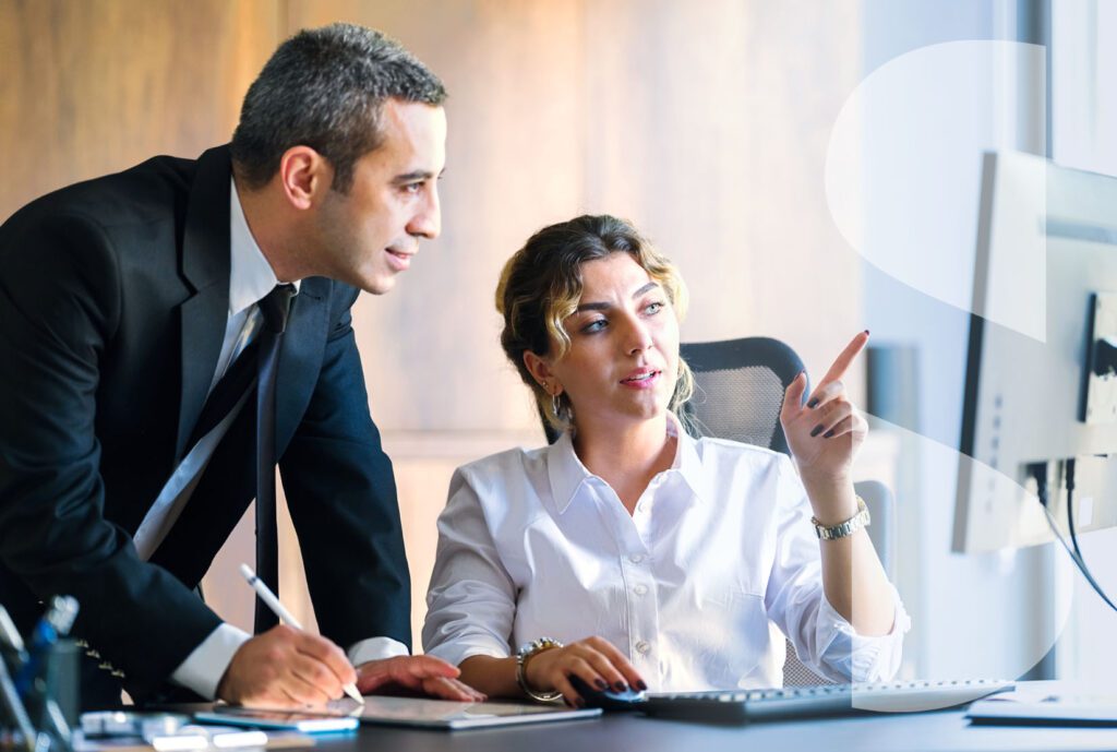 A male manager takes notes while a seated female colleague points at a desktop monitor. A white semi-transparent ImageSource icon covers the right side of the frame.